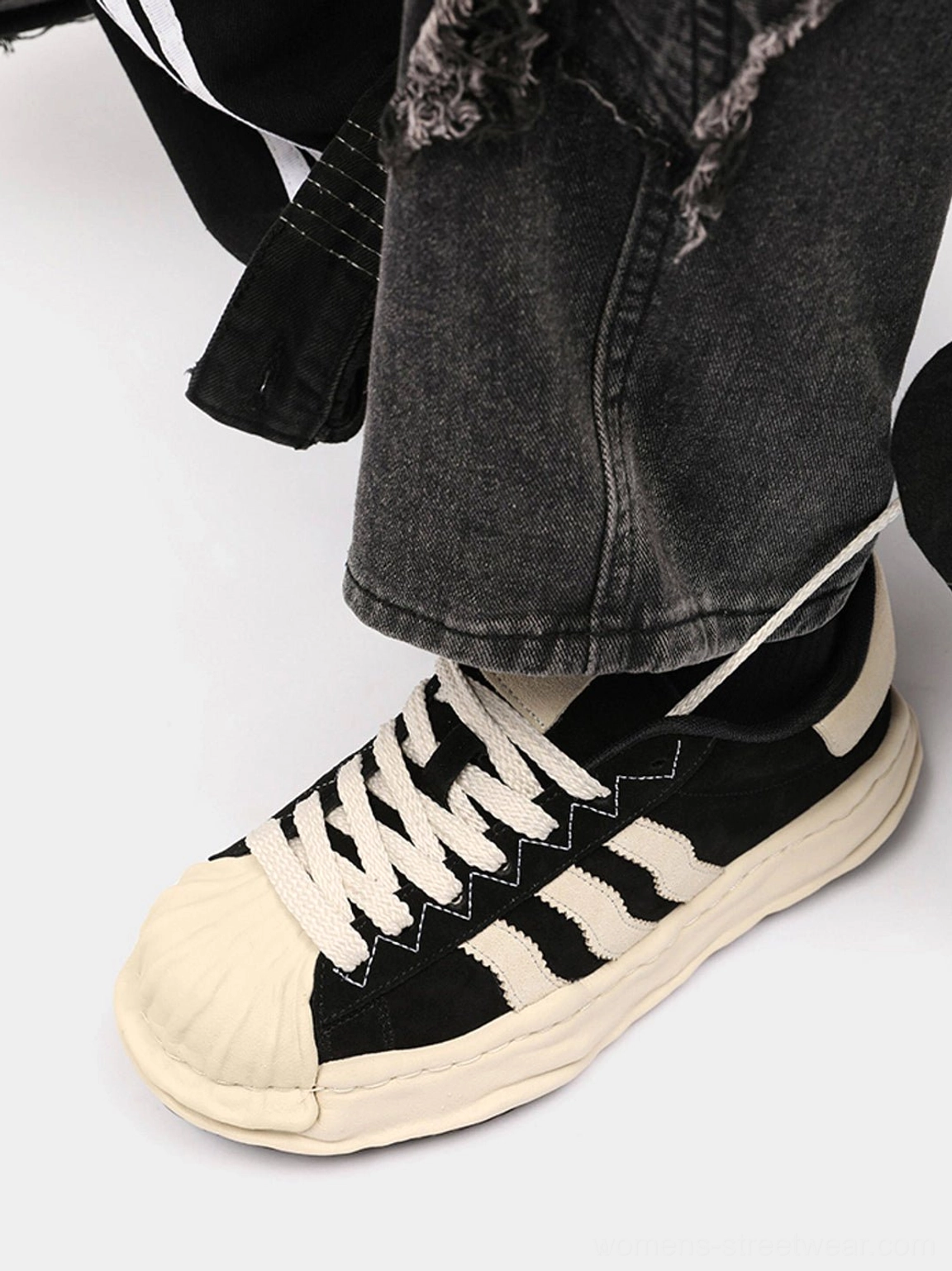Side close-up of black melted platform sneakers showing the off-white shell toe, contrast side stripes, and thick aged-style outsole