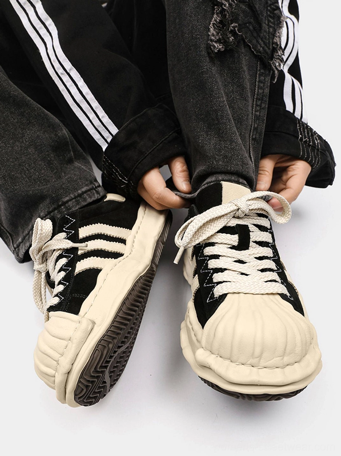 Top-down styling view of black melted shell-toe platform sneakers paired with ripped denim and side-stripe track pants