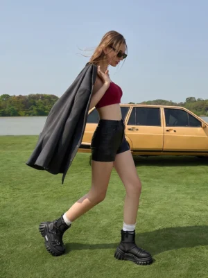 Woman wearing black mesh-cuff platform combat boots with shorts and cropped top in an outdoor streetwear editorial setting