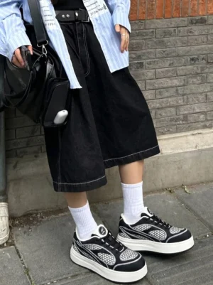 Model wearing black mesh platform derby sneakers with white crew socks, cropped denim skirt, and crossbody bag on an urban brick sidewalk