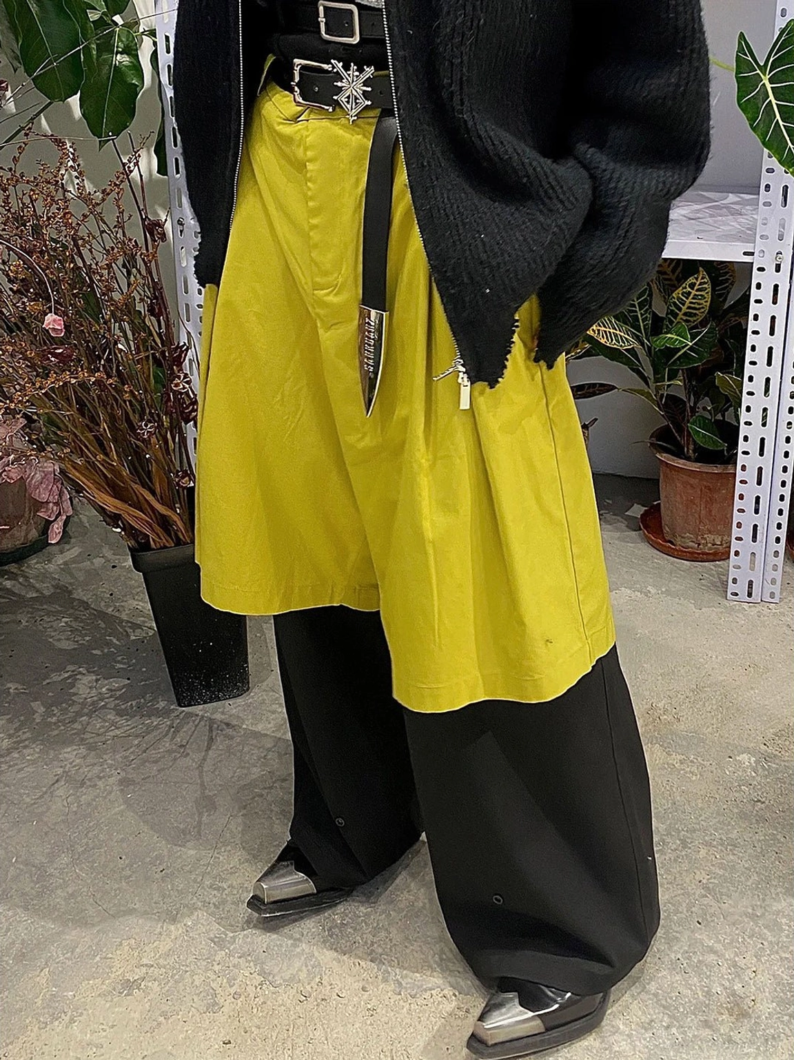 Front low-angle view of black metallic toe block heel Chelsea boots worn with color-block wide-leg pants and a dark streetwear outfit