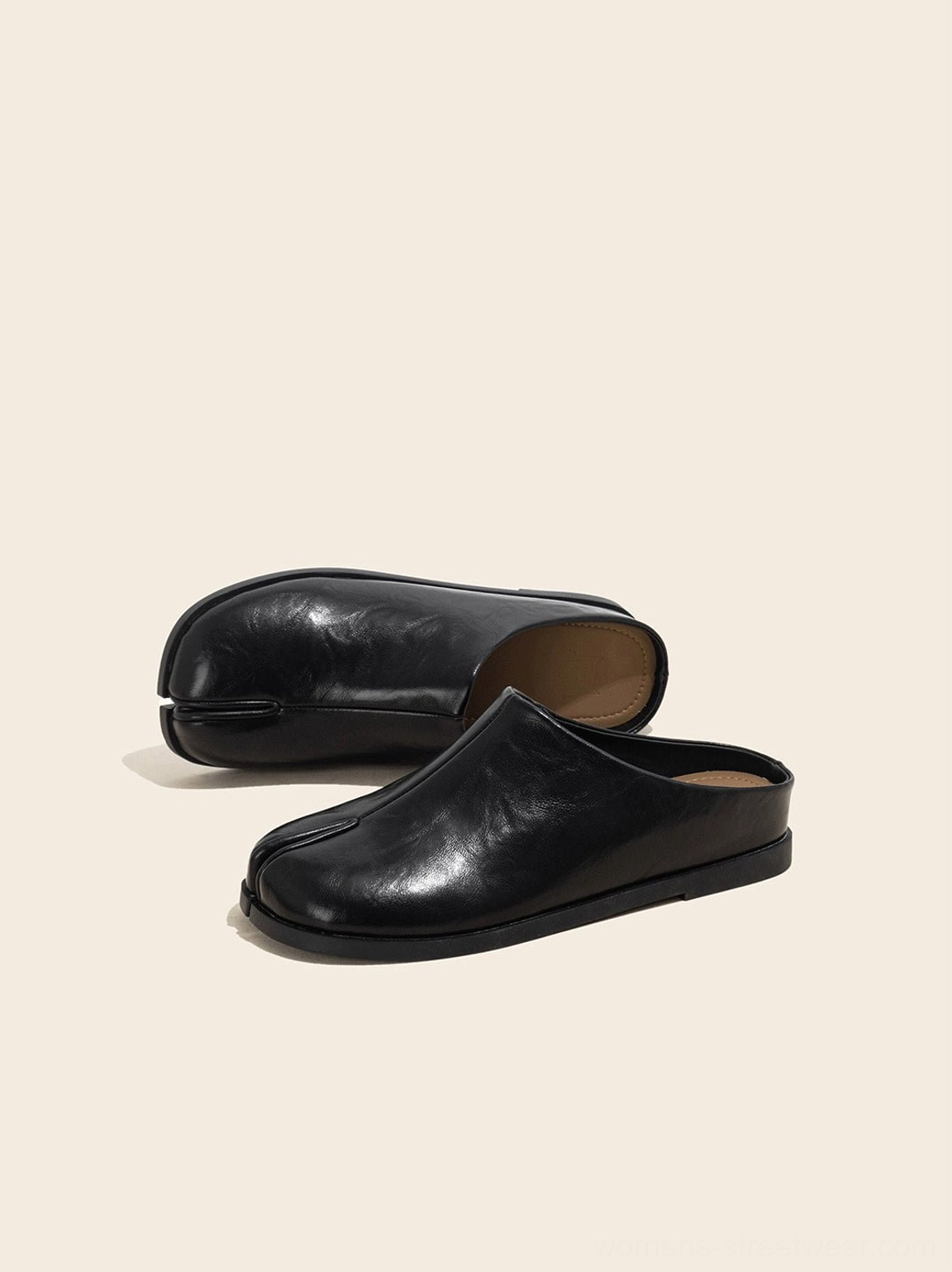 Black minimalist leather mules displayed horizontally to highlight the smooth upper and split-toe shape