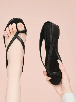 Close-up of black low wedge toe ring flip-flop sandal worn on foot against a soft pink background