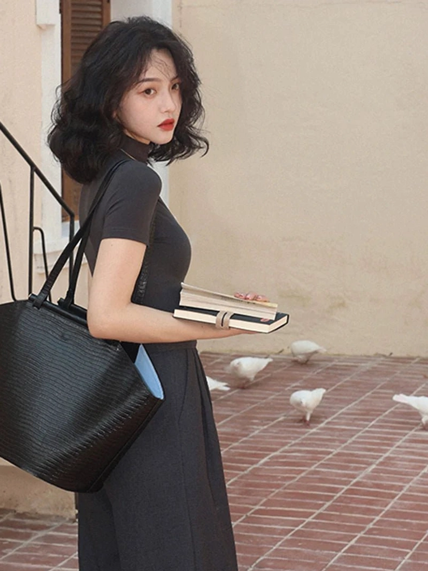 Woman styling a black mock neck short sleeve Korean streetwear top with a dark long skirt leather tote bag and books