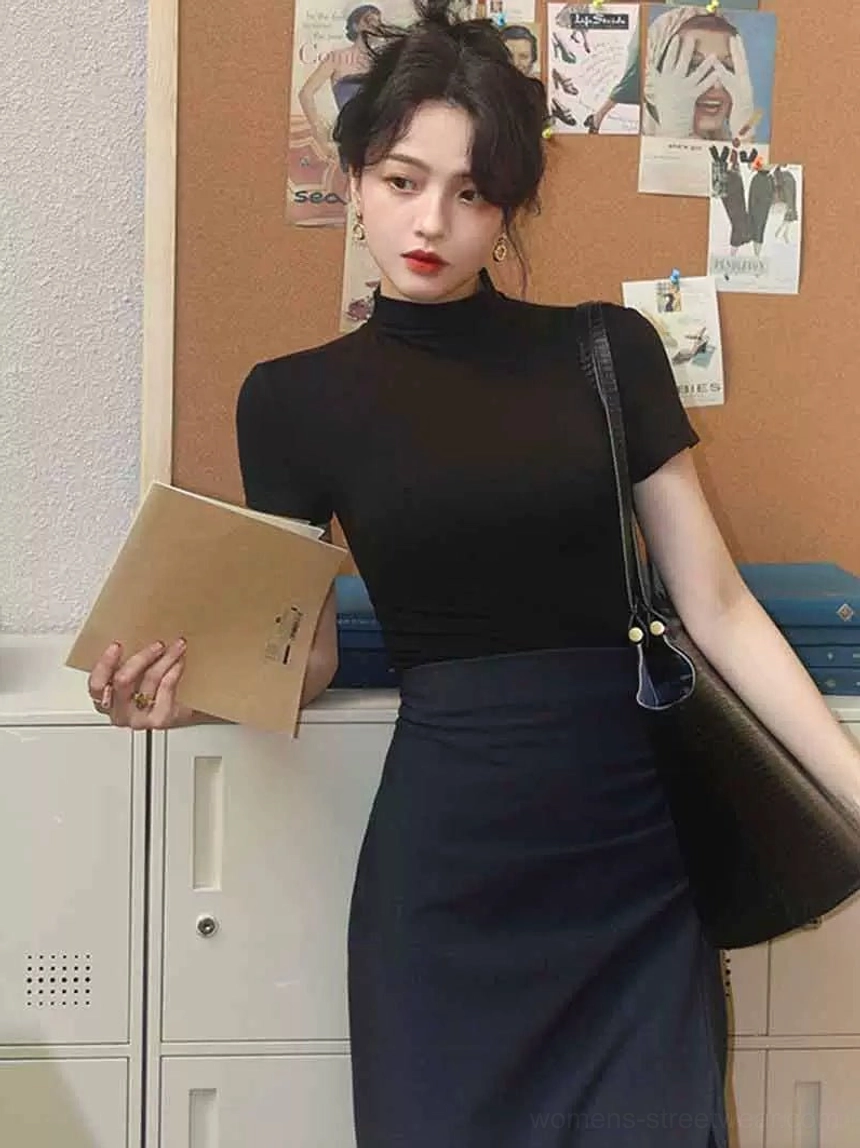 Woman wearing a black mock neck short sleeve minimalist top with a high waisted dark midi skirt leather tote and brown folder