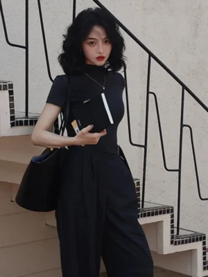 Woman wearing a black mock neck short sleeve slim fit streetwear top with high waisted dark wide leg trousers and tote bag on an outdoor staircase