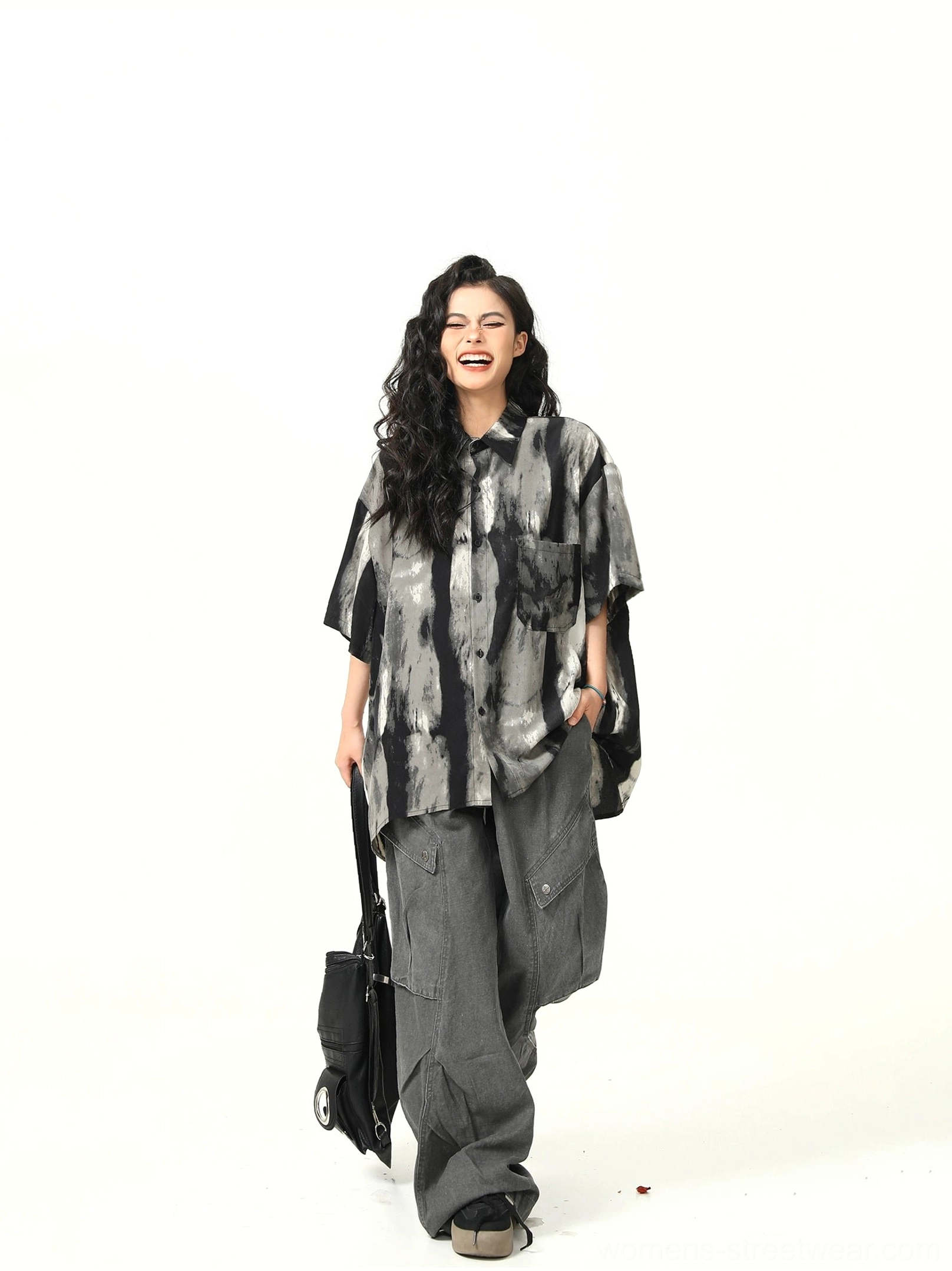 Side front view of a woman wearing a loose black monochrome watercolor button-up shirt with curved hem and cargo pants