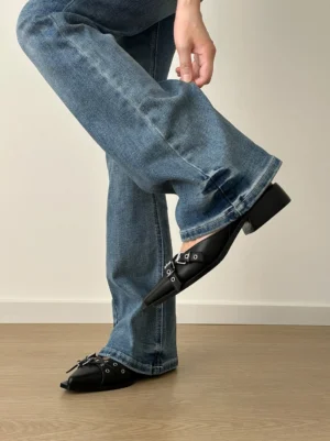 Black multi-buckle pointed Mary Jane flats worn with blue flared jeans in a side rear streetwear styling view