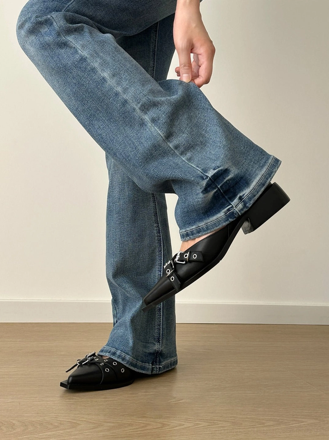 Black multi-buckle pointed Mary Jane flats worn with blue flared jeans in a side rear streetwear styling view