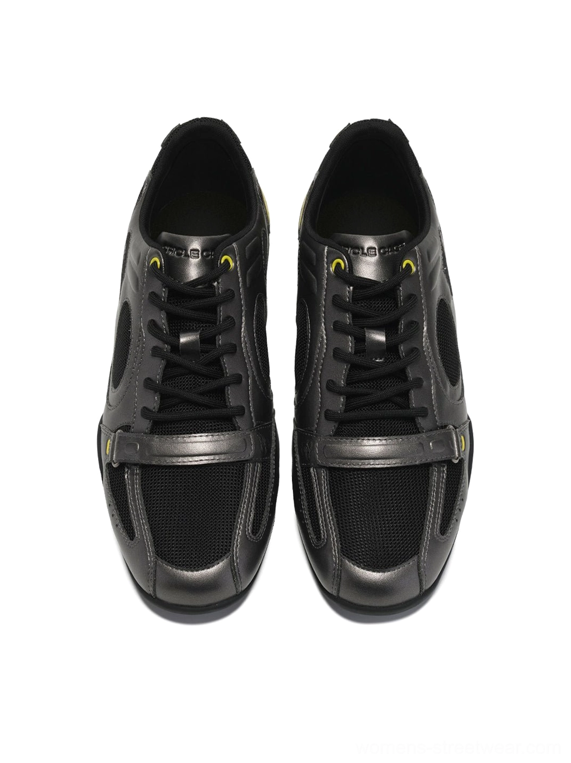 Black retro colorblock sneakers displayed on a metal stand showing the upper construction, insole, laces, and neon yellow heel detail