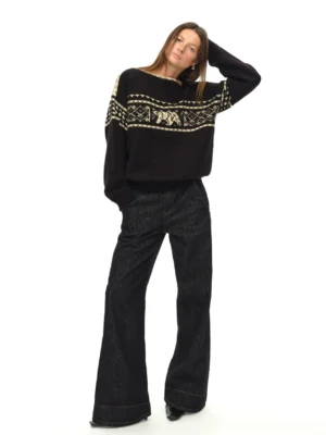 Black Nordic bear jacquard off-shoulder oversized knit sweater shown in left three-quarter full-body view with dark wide-leg jeans