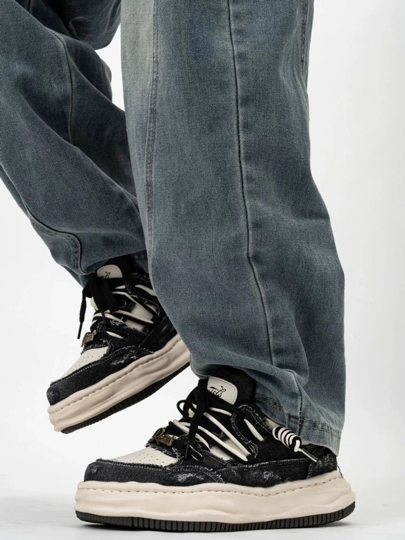 Black and off white distressed skate sneakers with thick cream midsole layered laces and chunky streetwear silhouette shown from the rear