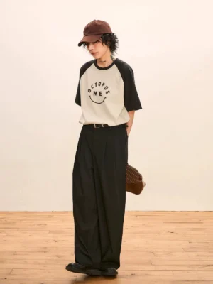 Black and off-white raglan graphic tee styled with black wide-leg trousers and a brown newsboy cap