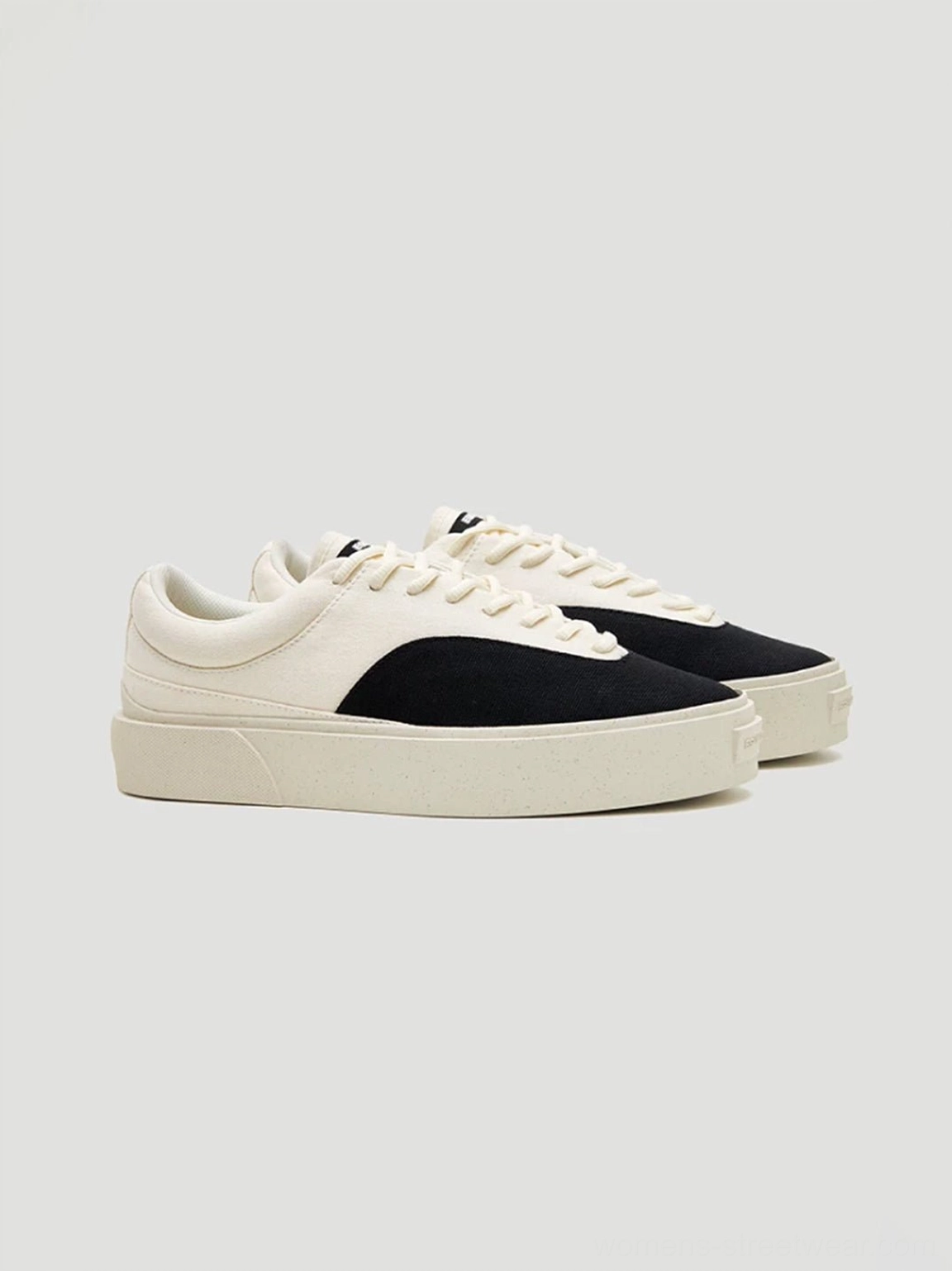 Angled pair view of two-tone black and off-white canvas skate shoes with low-top silhouette and thick egret white platform sole