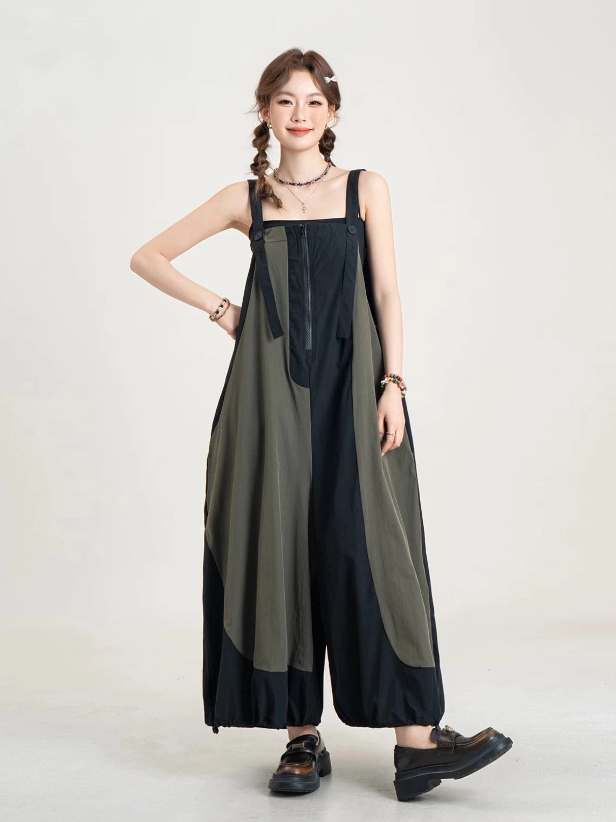 Front view of a black and olive color-block balloon-leg streetwear jumpsuit with adjustable straps, front zipper, oversized wide legs, and drawcord cuffs