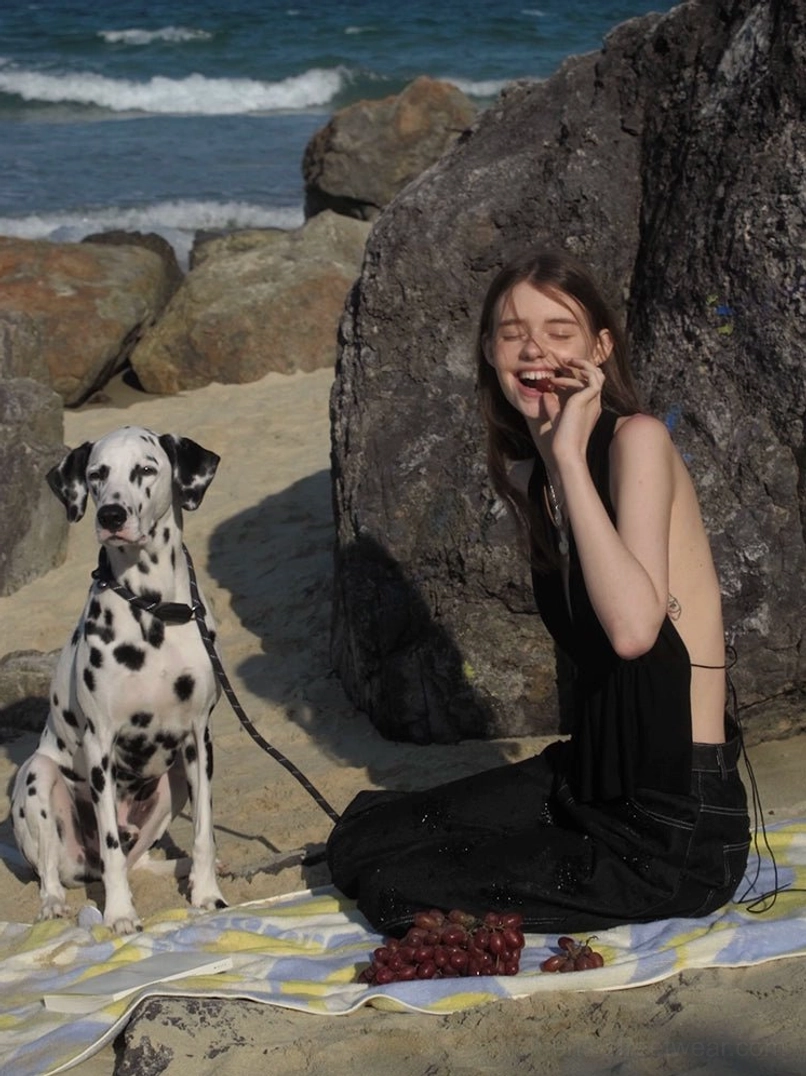Black open-back halter top styled with high-waisted wide-leg pants beside a rocky beach and Dalmatian dog
