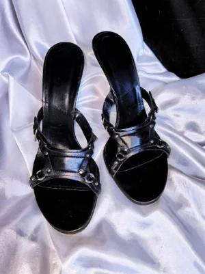 Black open-toe stiletto mule sandals with polished synthetic straps, metal rings, and rivet details shown from above