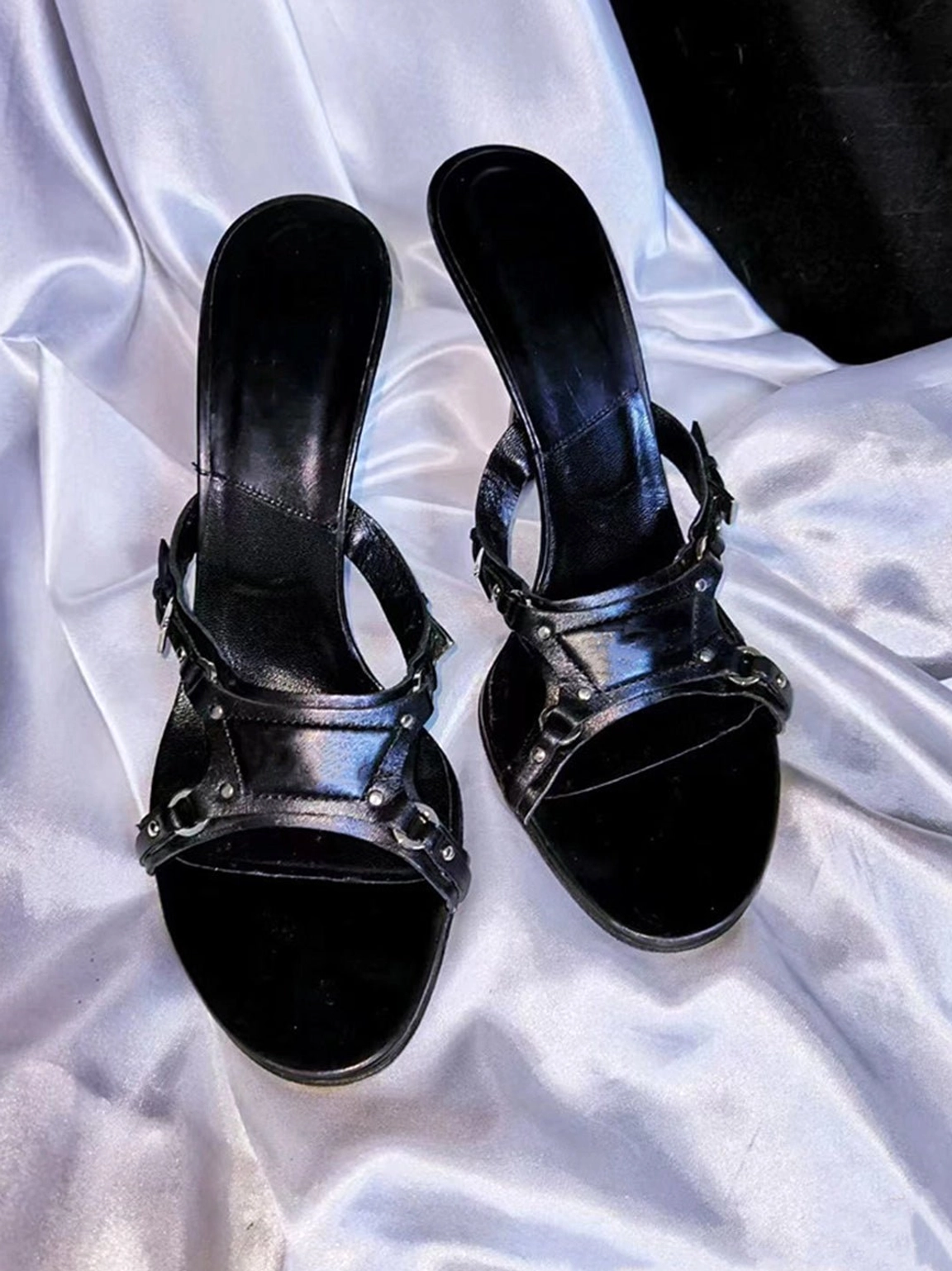 Black open-toe stiletto mule sandals with smooth synthetic upper and decorative metallic straps photographed from an overhead view