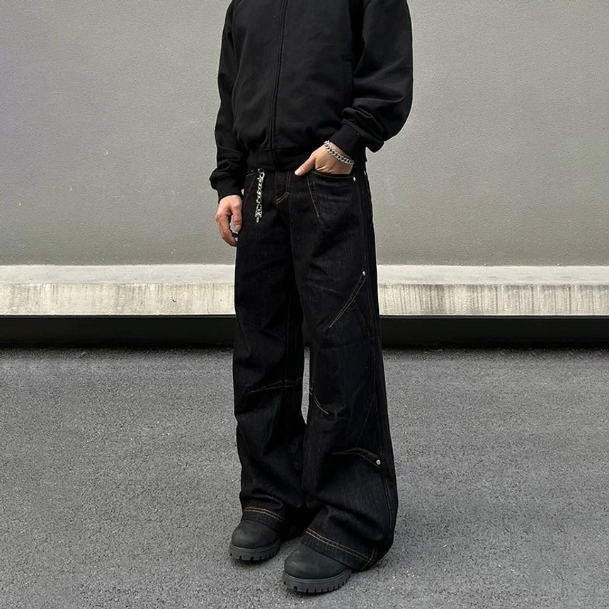 Close front view of black orbit panel baggy jeans with diagonal structured seams, front waistband detail, and relaxed wide-leg fit