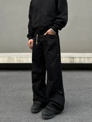 Front low-angle view of black orbit panel baggy wide-leg streetwear jeans with contrast stitching, chain accent, and black work boots