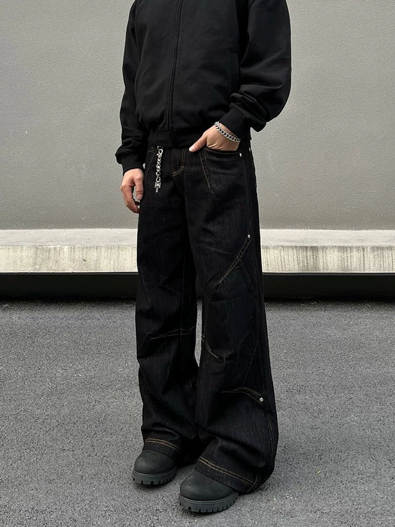 Front low-angle view of black orbit panel baggy wide-leg streetwear jeans with contrast stitching, chain accent, and black work boots