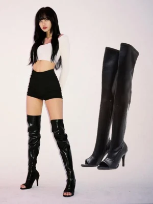 Woman wearing black over-the-knee patent stiletto boots with cropped white top and black shorts in a minimalist studio streetwear outfit