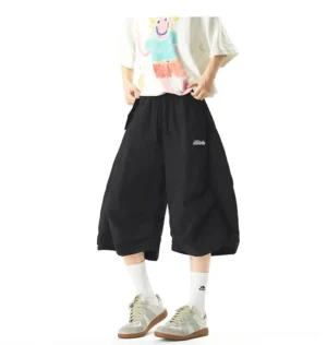 Black oversized balloon jogger shorts with wide cropped legs, elastic drawstring waist, side pockets, and embroidered detail styled with a graphic streetwear tee and retro sneakers