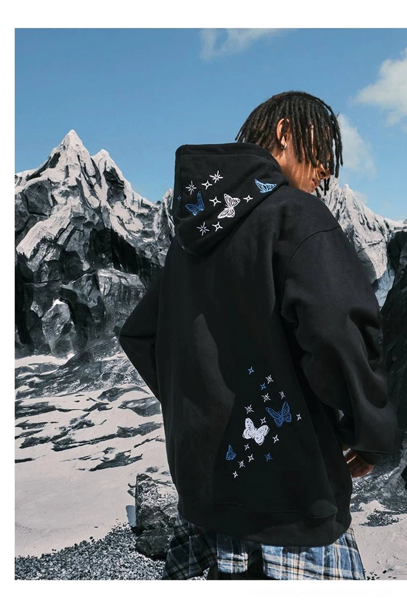 Male model wearing an all-Black oversized butterfly and star embroidered hoodie viewed from the back outdoors