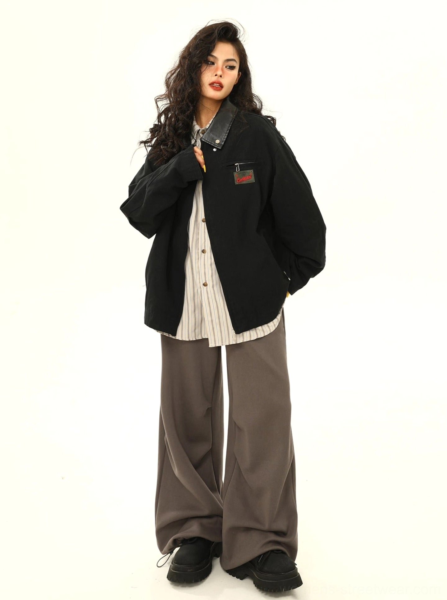 Full-body black oversized cargo work jacket styled over a striped shirt with contrast collar, relaxed sleeves, and casual sneakers