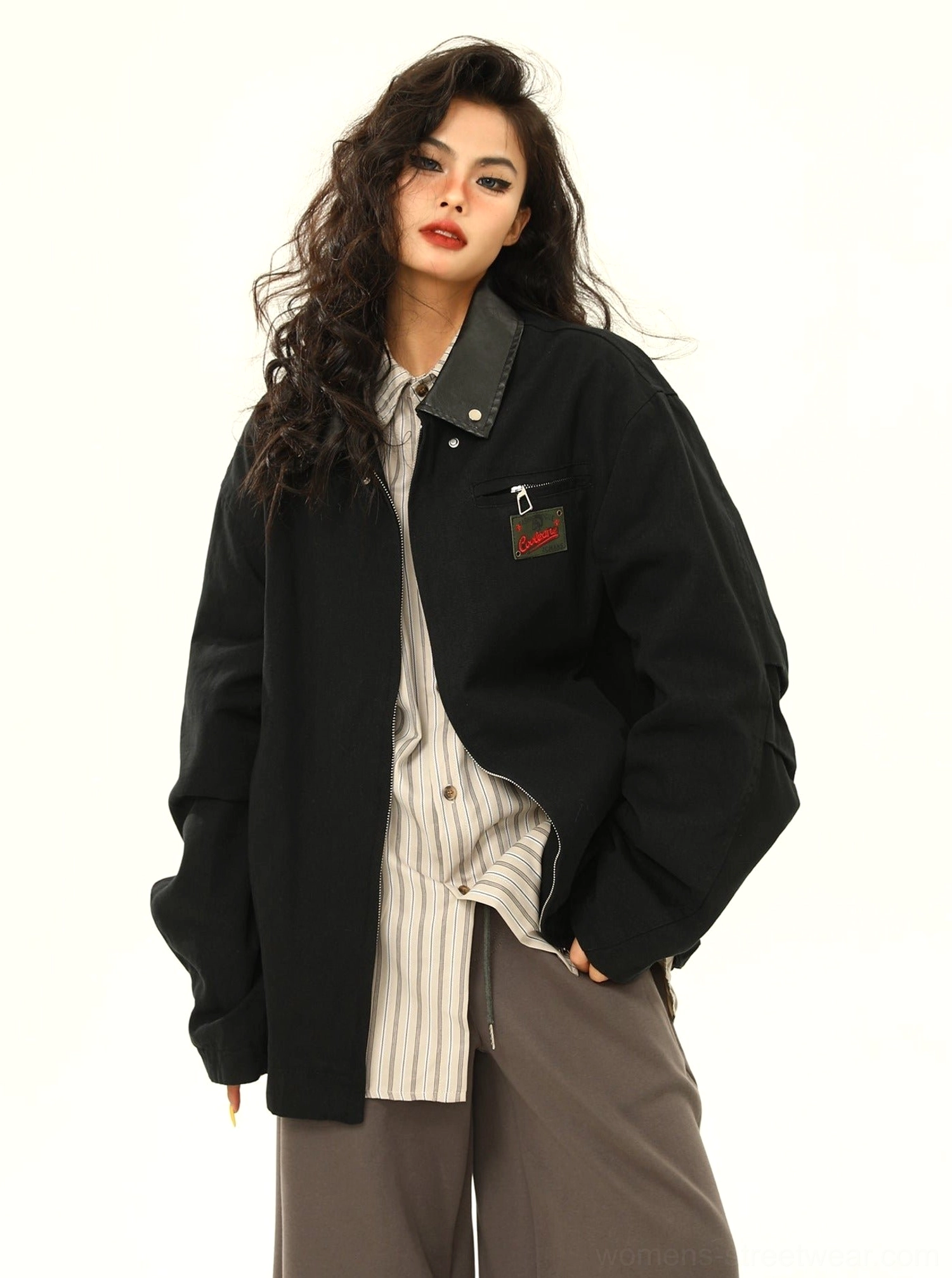 Three-quarter view of a black oversized cargo work jacket with dark contrast collar, embroidered chest patch, relaxed shoulders, and clean hemline