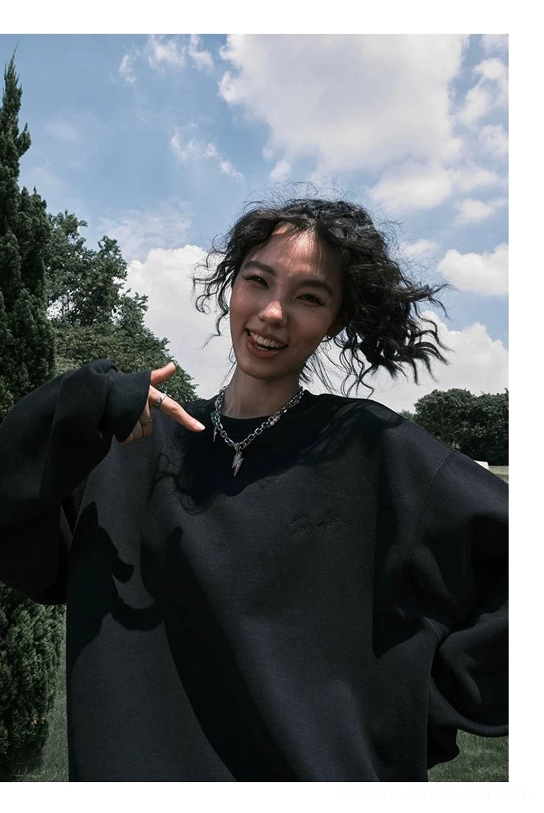 Front close-up of a black oversized crewneck sweatshirt with subtle front embroidery styled with layered silver necklaces