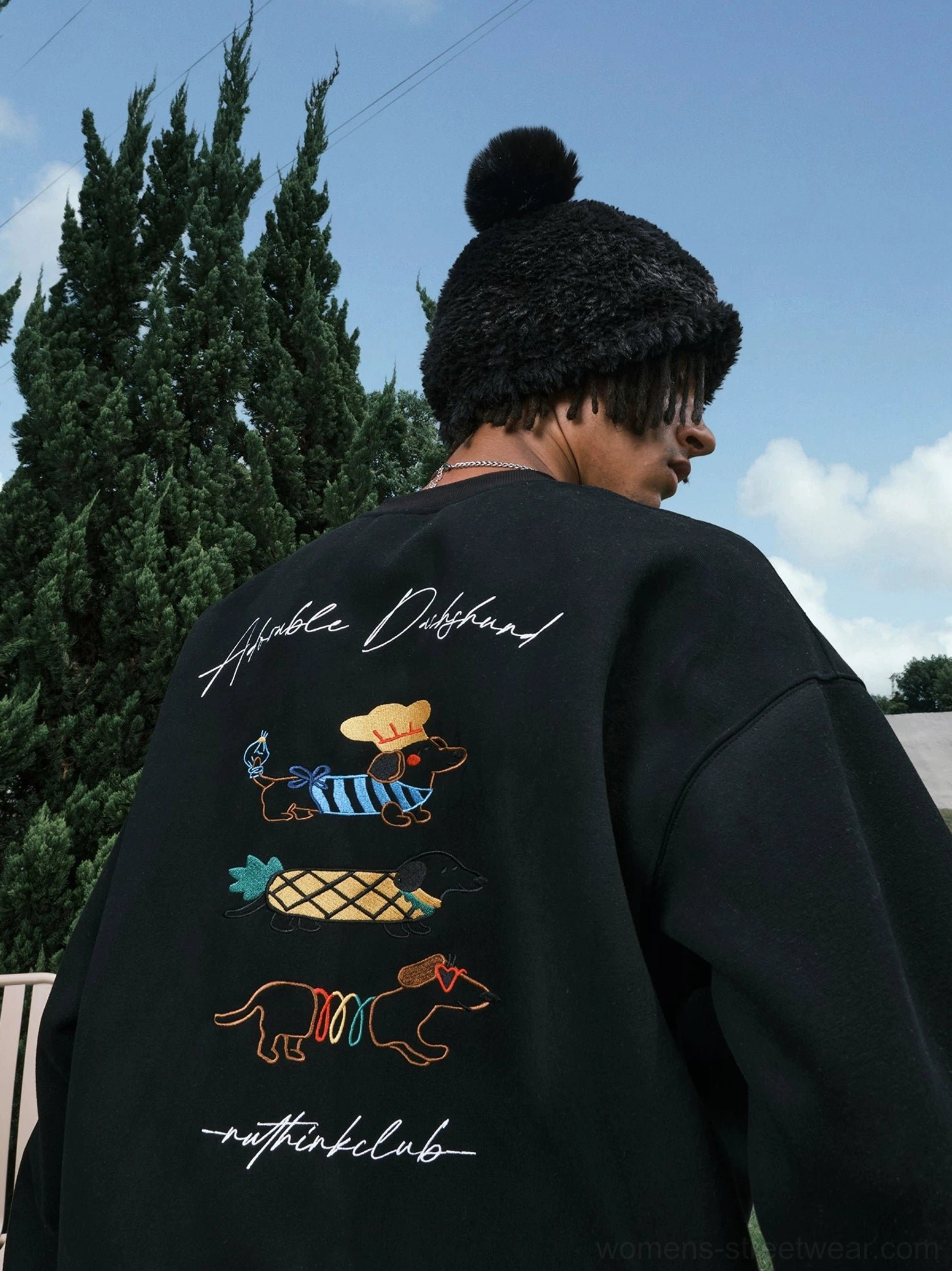 Black oversized dachshund graphic sweatshirt on a model wearing a pom-pom beanie with colorful back artwork and handwritten streetwear lettering