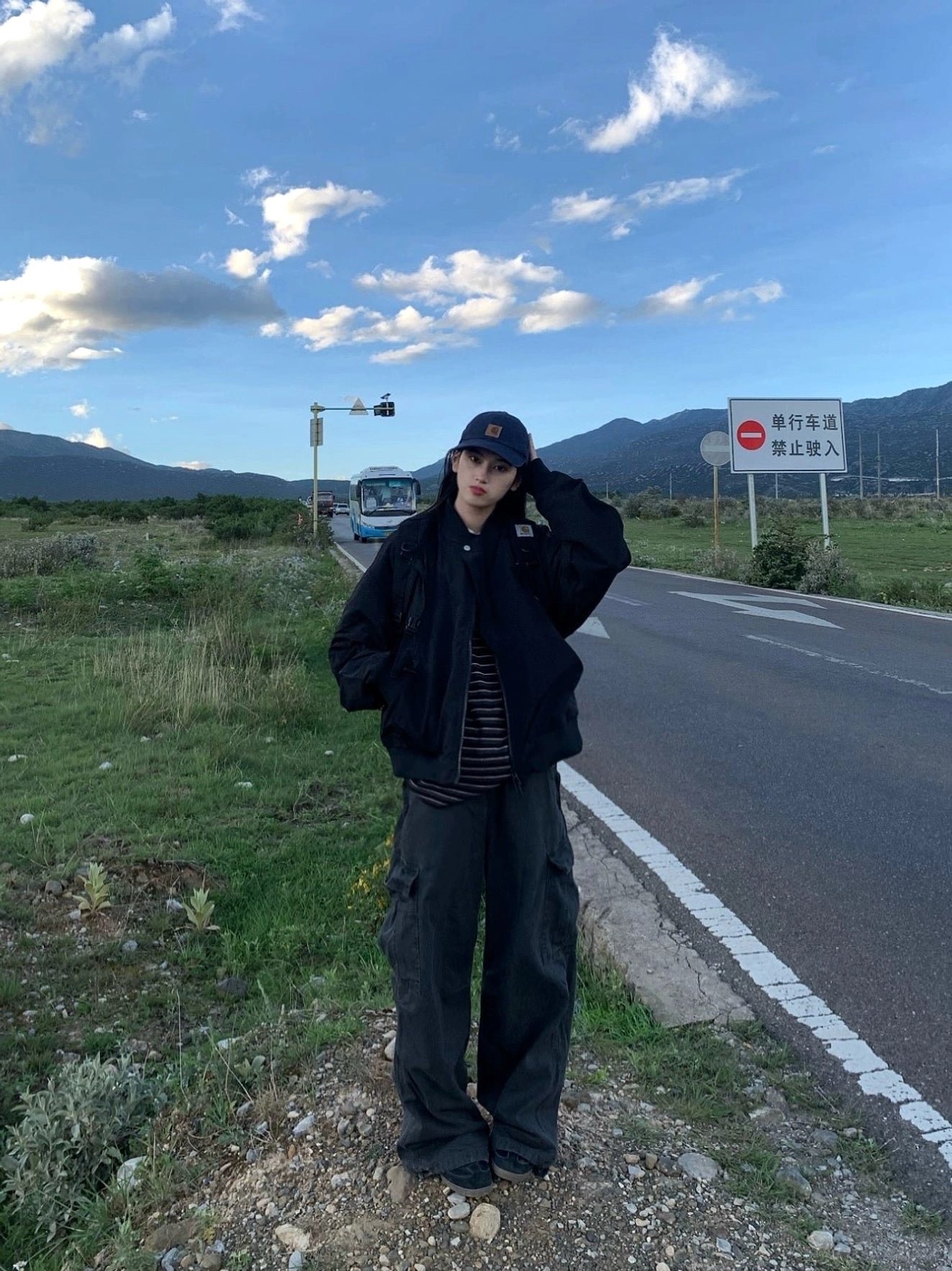 Black oversized flight jacket with striped inner layer and dark cargo pants on a rural roadside