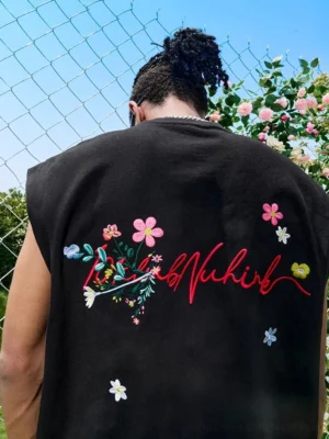 Close-up back view of black oversized floral embroidered muscle tank top with colorful flowers and flowing script streetwear graphic