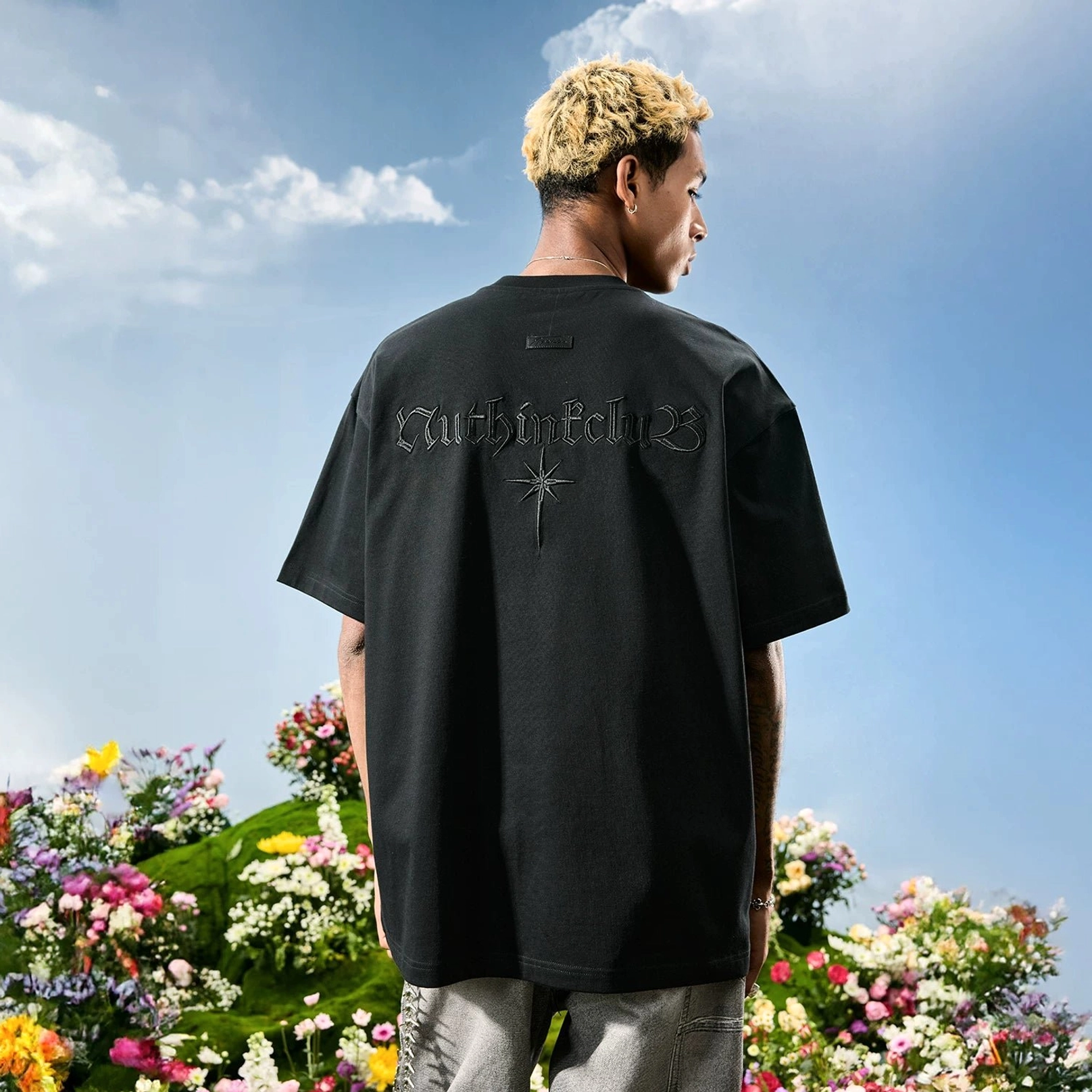 Black oversized Gothic embroidered T-shirt on male model with hands in pockets, showcasing the back graphic and relaxed unisex fit