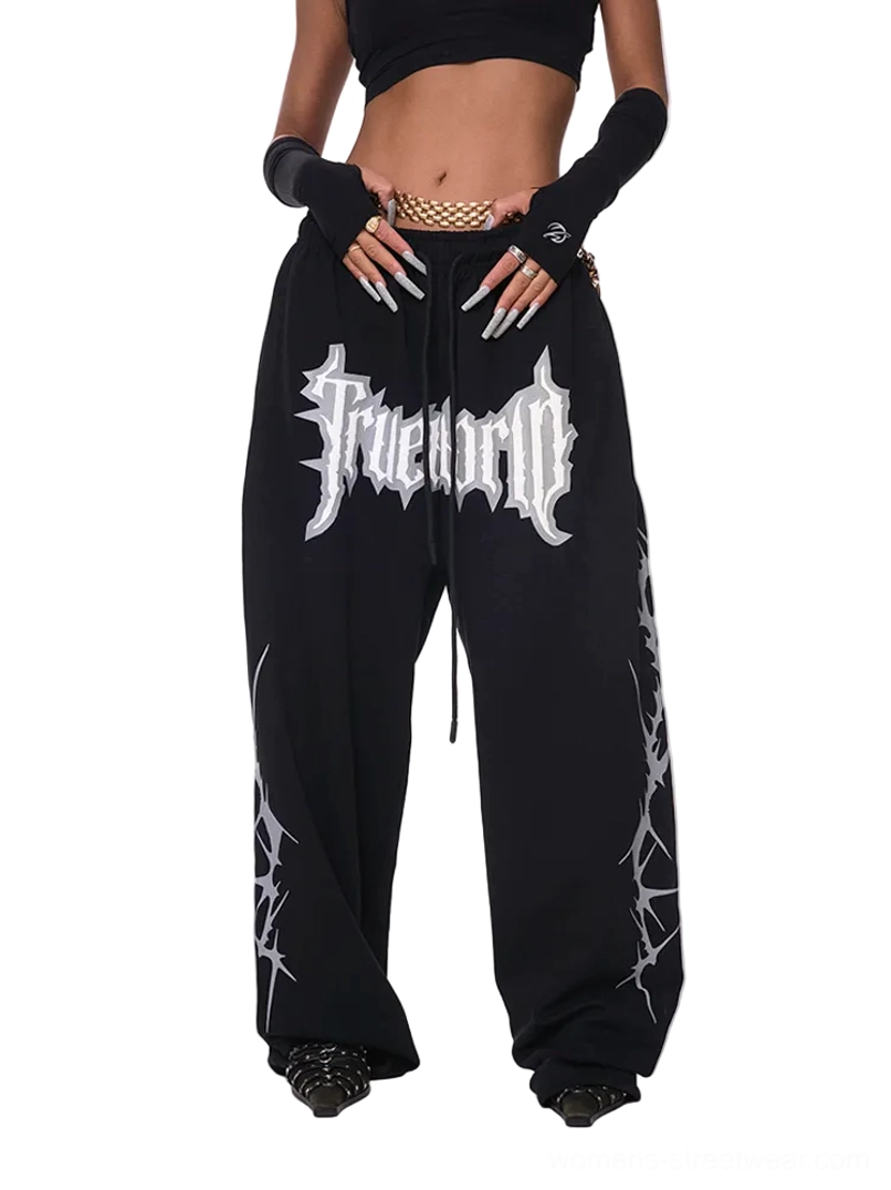 Black oversized gothic streetwear sweatpants with silver front graphic, wide-leg stacked fit, adjustable drawstring waist, and thorn-inspired side patterns