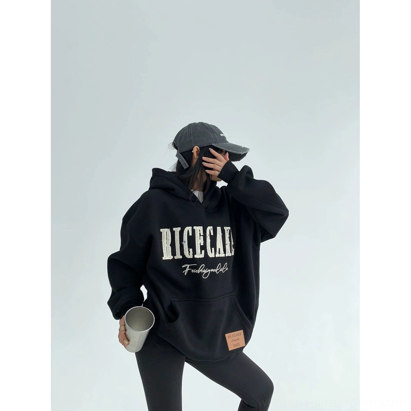Black oversized graphic hoodie styled with baseball cap and black leggings, showcasing a relaxed monochrome streetwear silhouette
