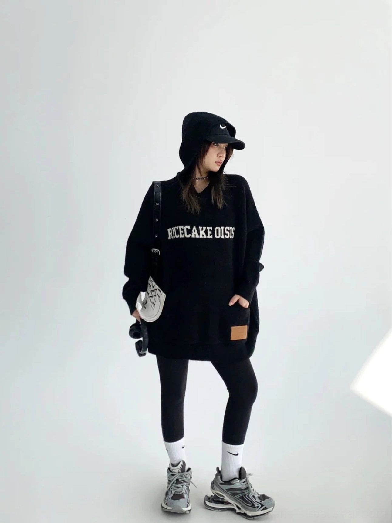 Black oversized graphic knit hoodie styled with a black bucket hat, leggings, sporty sneakers, and leather hem patch