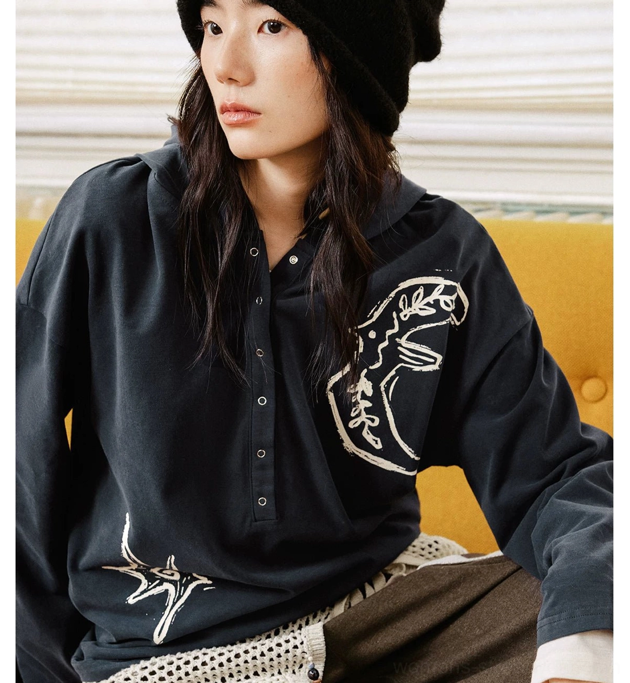 Front close-up of black oversized Henley polo shirt with hand-drawn animal and star embroidery and half-button neckline