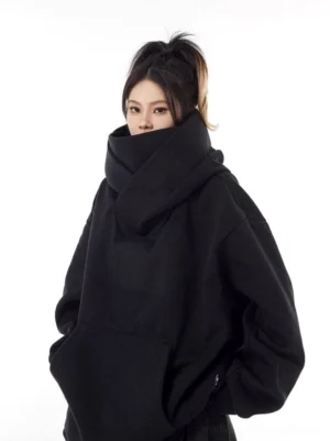 Front view of a black oversized high-neck hoodie with face-covering collar, soft fleece-like texture, and spacious kangaroo pocket