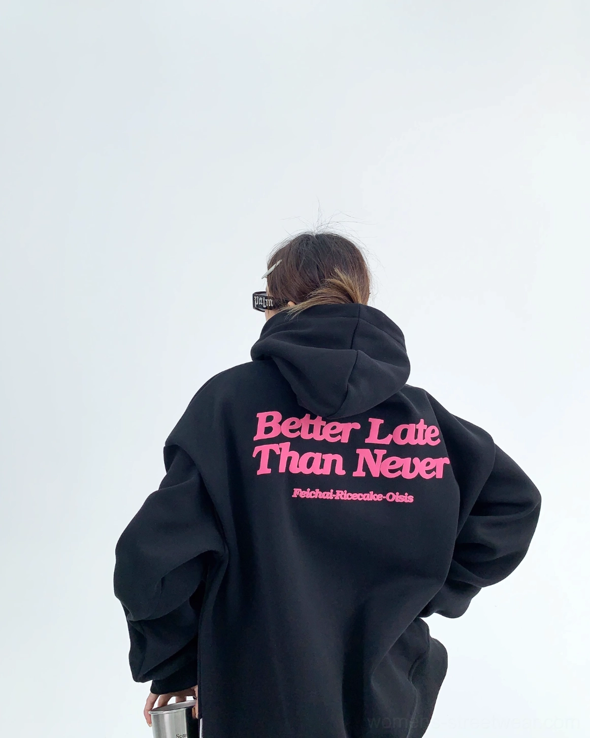 Jet black oversized graphic hoodie rear view with full pink Better Late Than Never slogan attached hood and relaxed silhouette