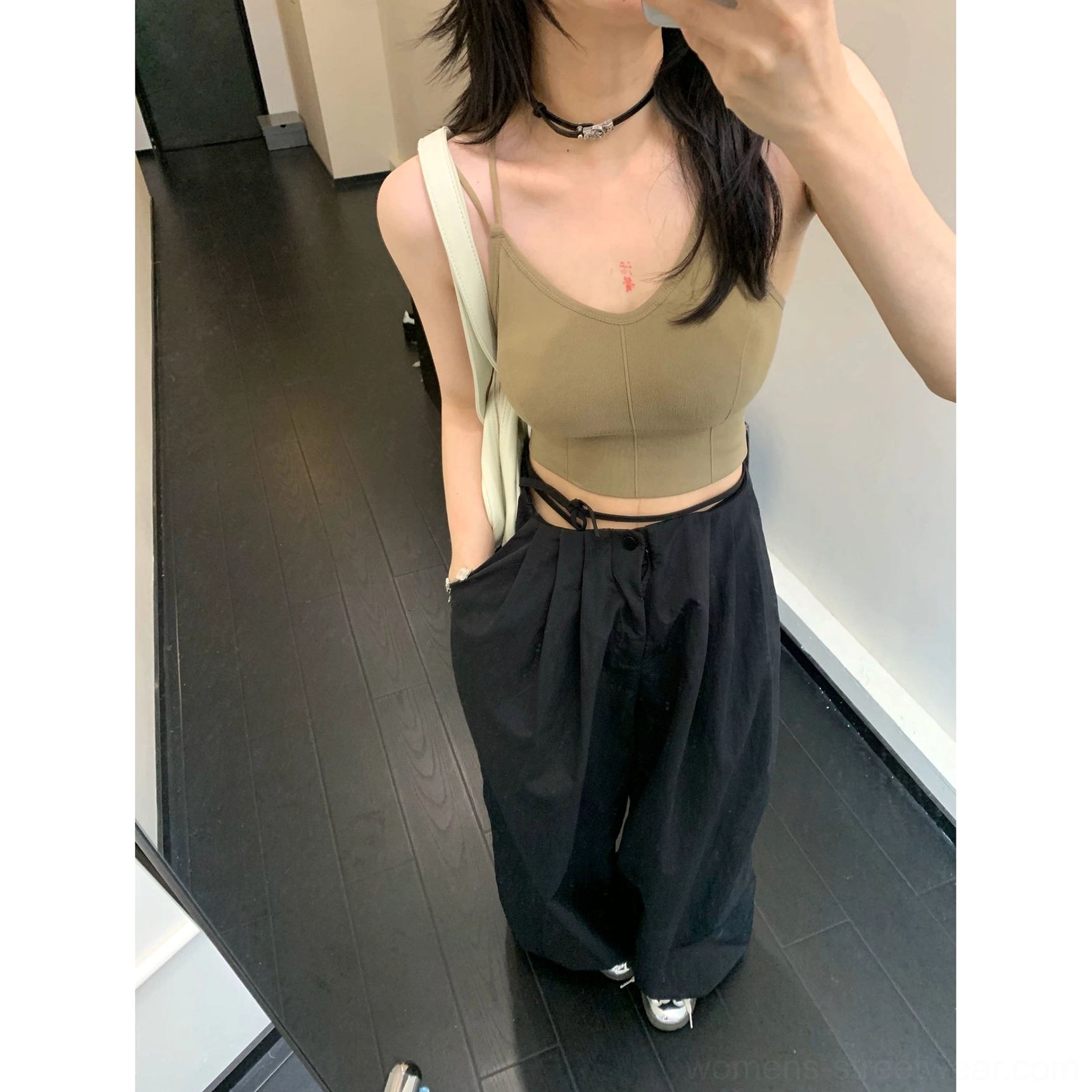 Black oversized parachute pants close-up showing the low-rise drawstring waist, exposed tie straps, and loose wide-leg cut