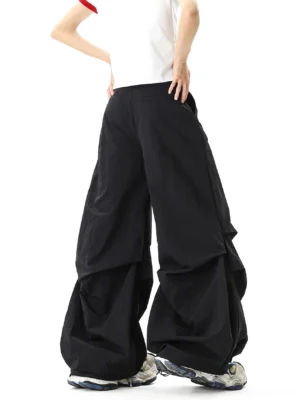 Rear view of oversized black parachute streetwear pants showing the relaxed wide-leg balloon silhouette, gathered fabric layers, and clean elastic back waistband