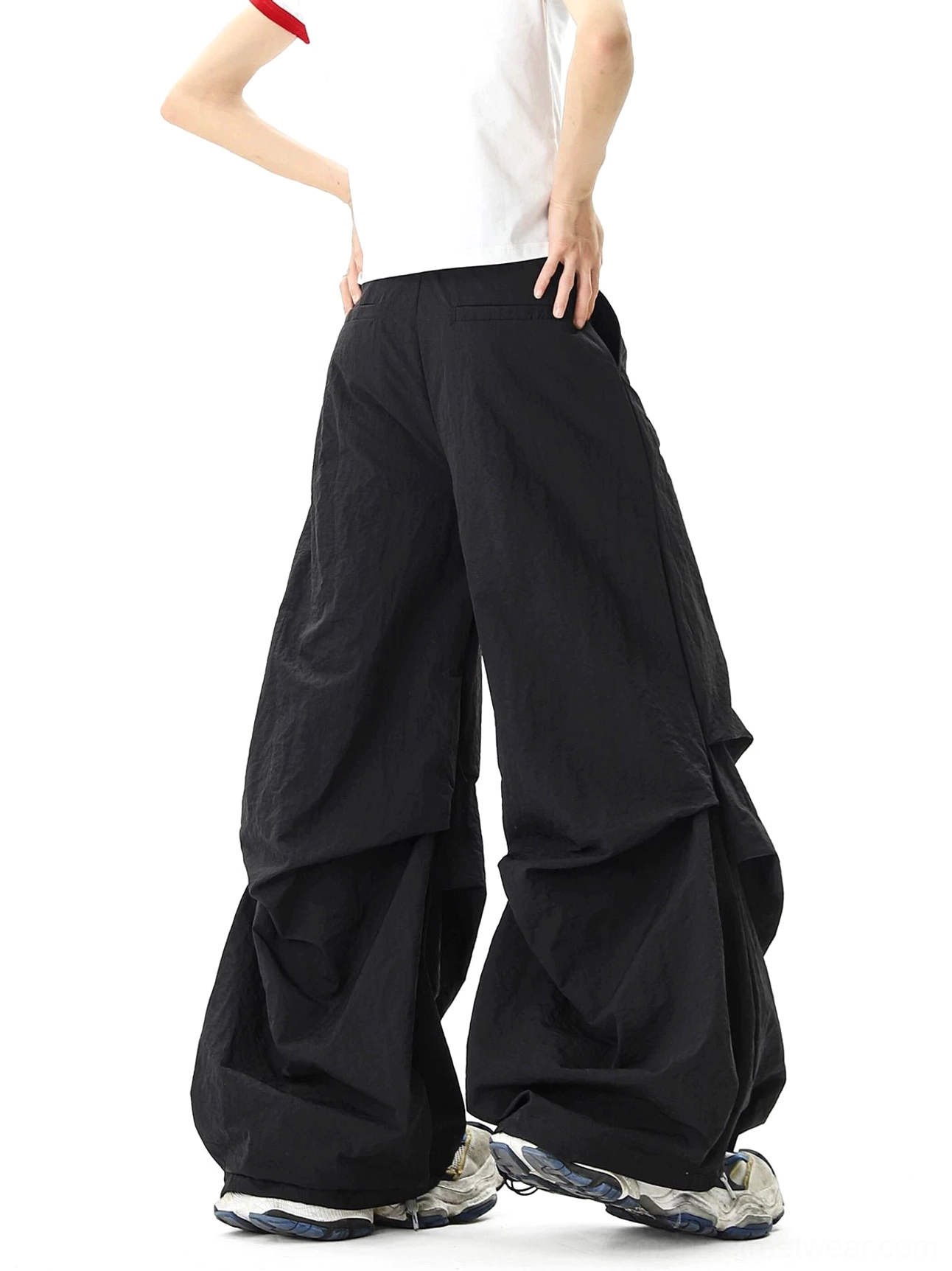 Rear view of oversized black parachute streetwear pants showing the relaxed wide-leg balloon silhouette, gathered fabric layers, and clean elastic back waistband