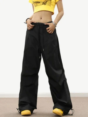 Black oversized parachute track pants with relaxed wide-leg fit, adjustable waist, and ankle toggles styled with a yellow cropped top
