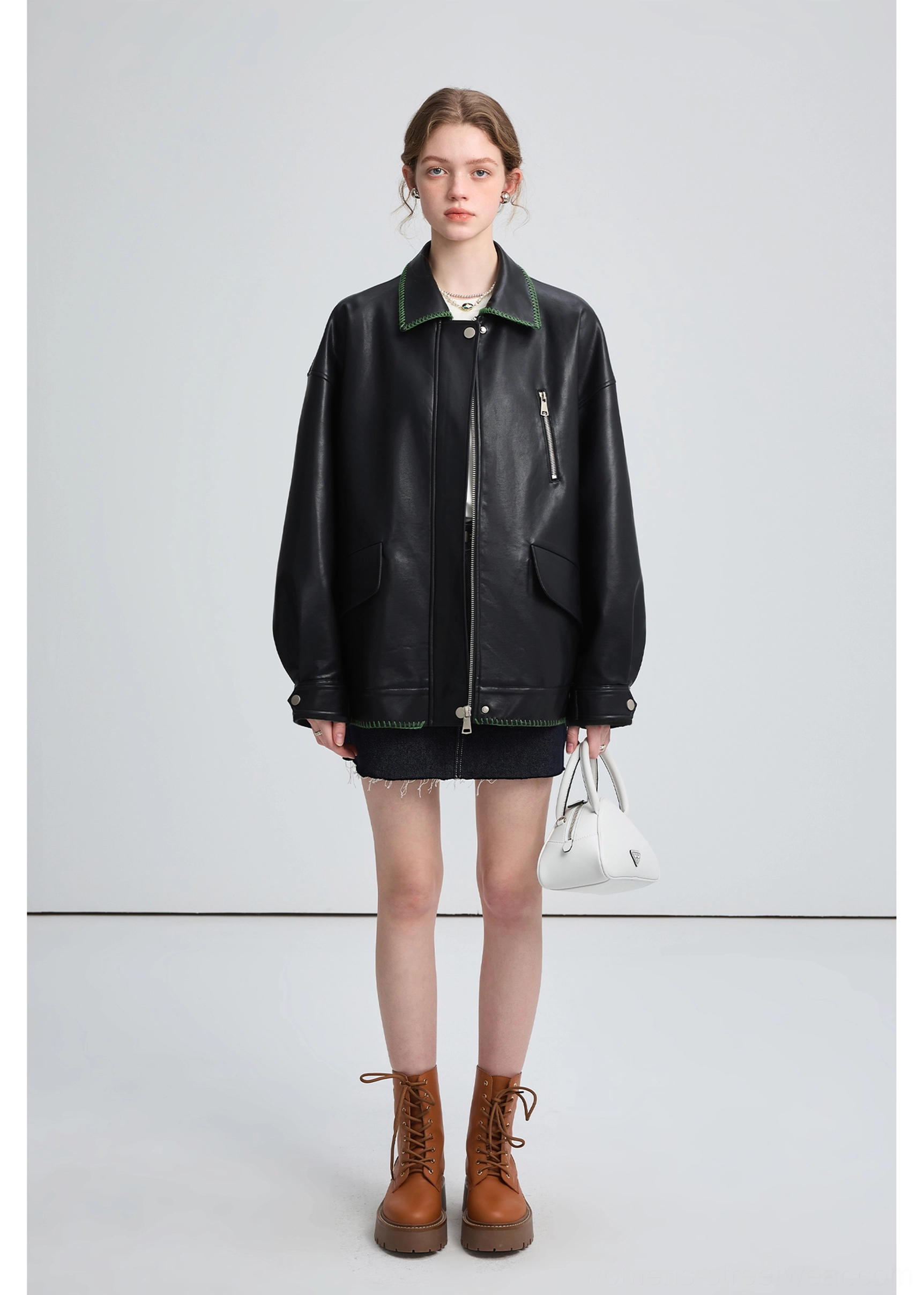 Front view of a black oversized PU leather biker jacket styled with a denim skirt, combat boots, and white handbag
