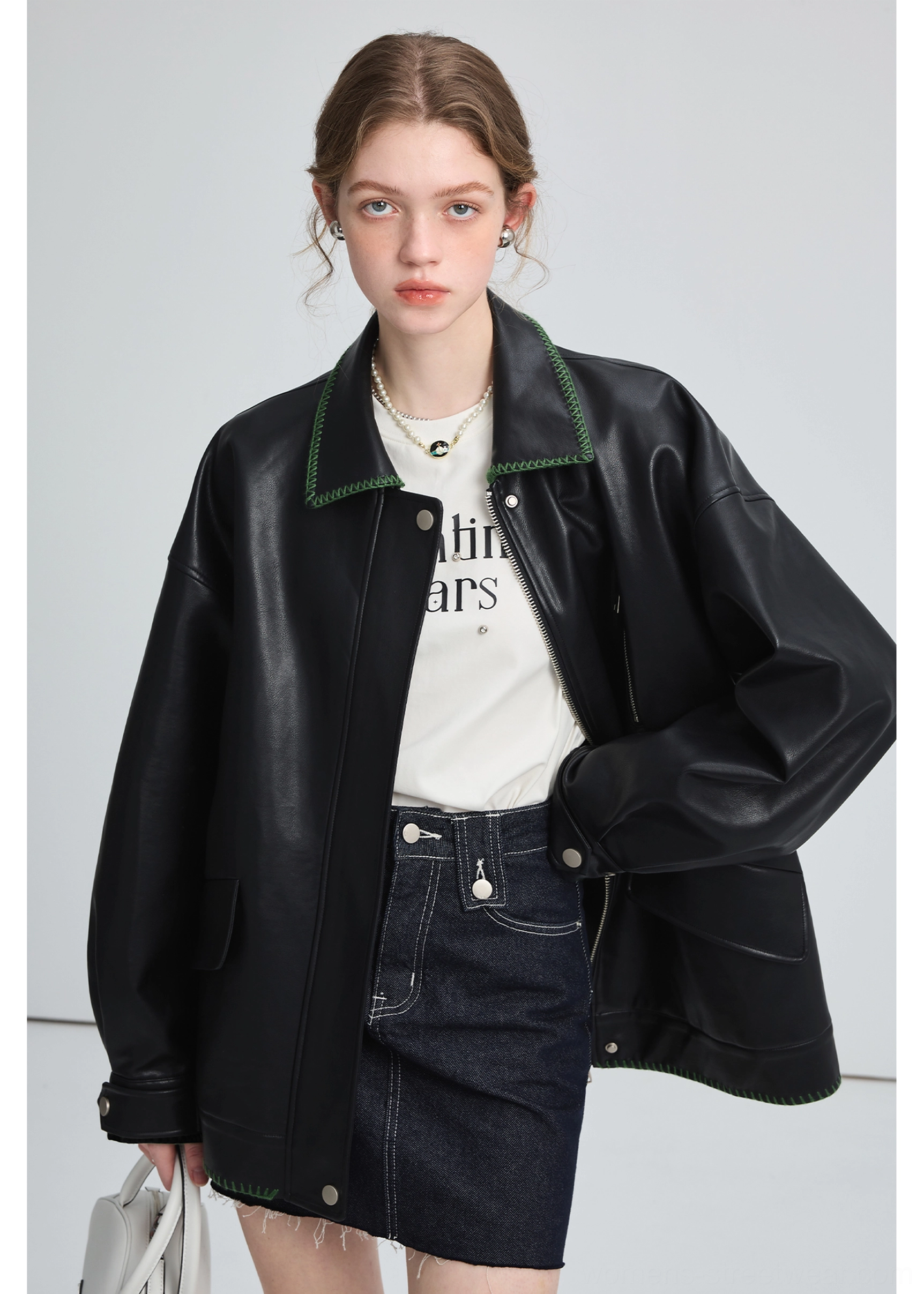 Model wearing a black oversized PU leather biker jacket with green contrast collar stitching in a relaxed streetwear outfit