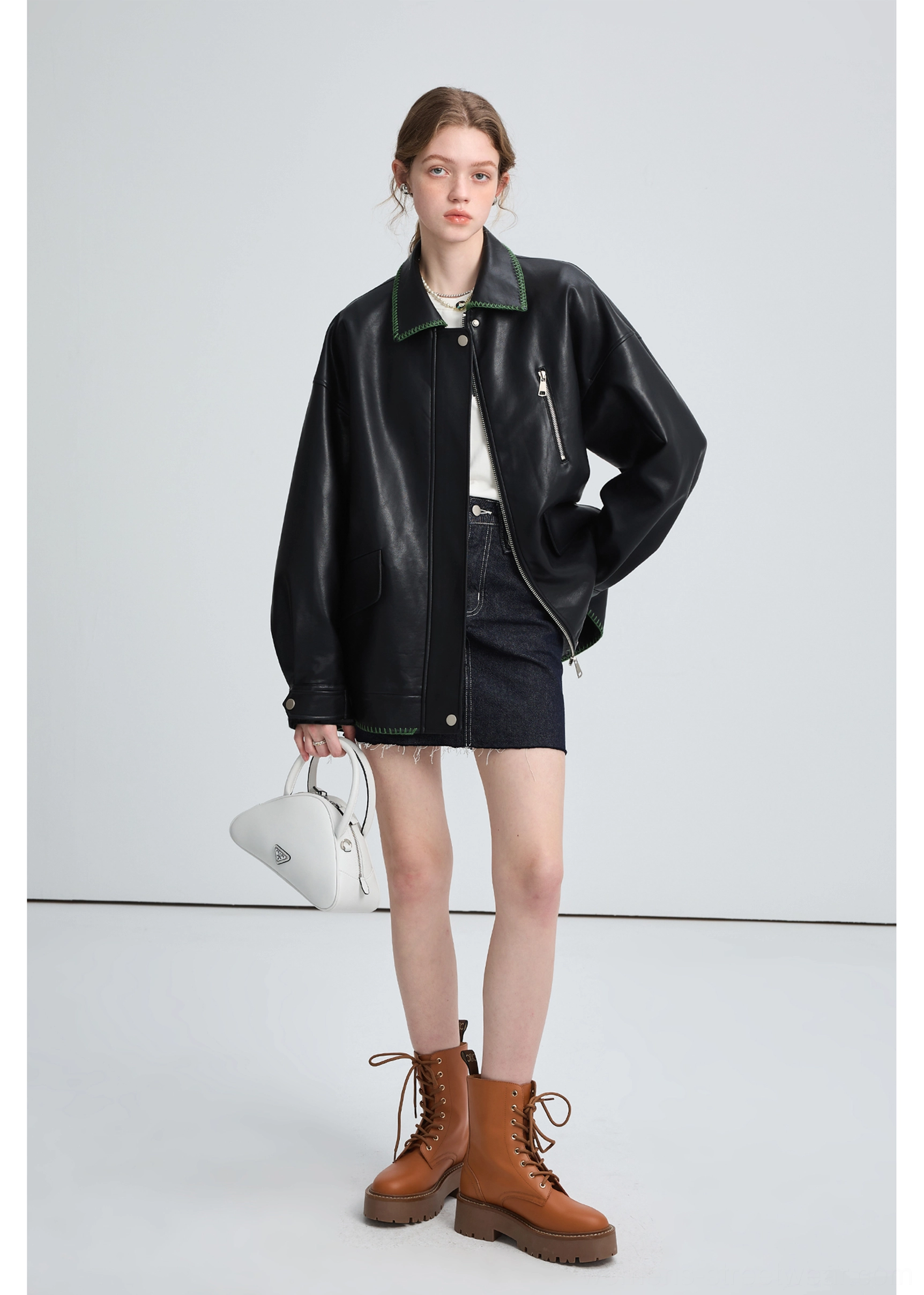 Three-quarter view of a black oversized PU leather biker jacket with smooth finish, green collar trim, and snap hem