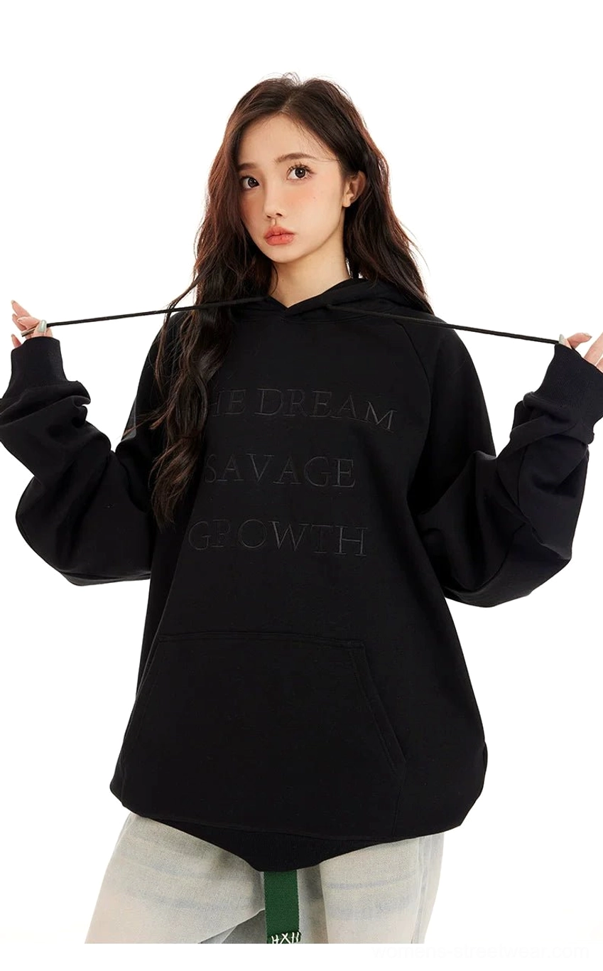 Black oversized pullover hoodie with tonal embossed lettering, dropped shoulders, adjustable drawstring hood, and long relaxed sleeves