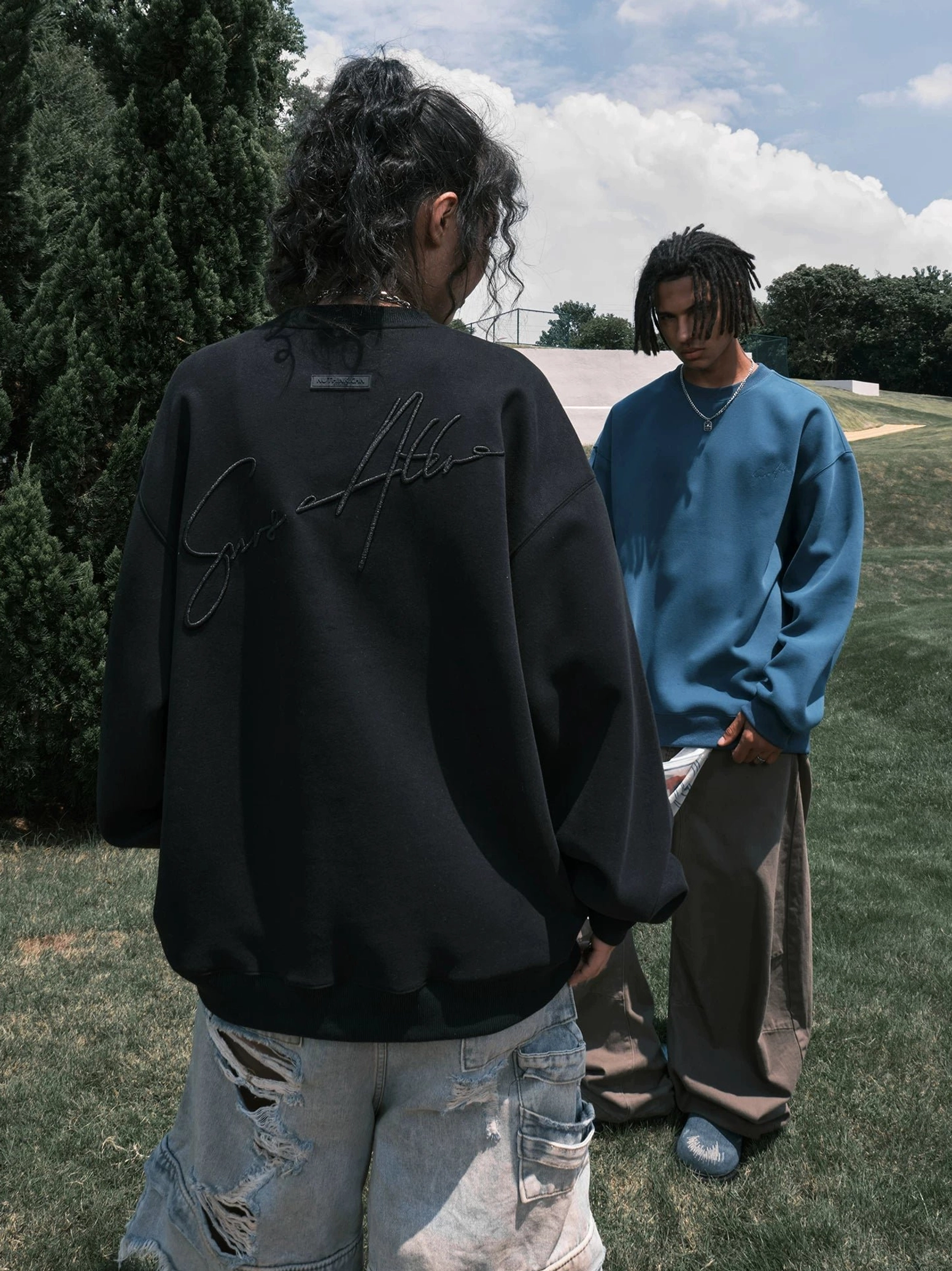 Female model wearing a black oversized script embroidered crewneck sweatshirt with ripped light wash denim shorts in a casual streetwear outfit